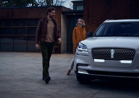 A man and a woman approaching a 2024 Lincoln Aviator® SUV, which illuminates certain lights when they are close | Krenzen Lincoln in Duluth MN