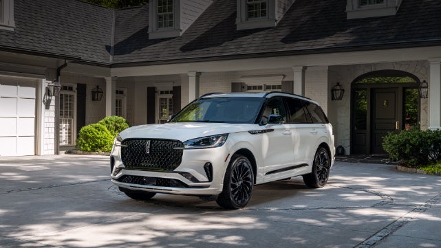 A white 2026 Lincoln Aviator® SUV is parked in the driveway of a luxury home. | Krenzen Lincoln in Duluth MN