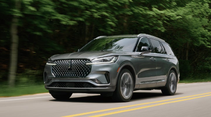 A 2027 Lincoln Aviator® SUV is being driven down a road lined with trees. | Krenzen Lincoln in Duluth MN